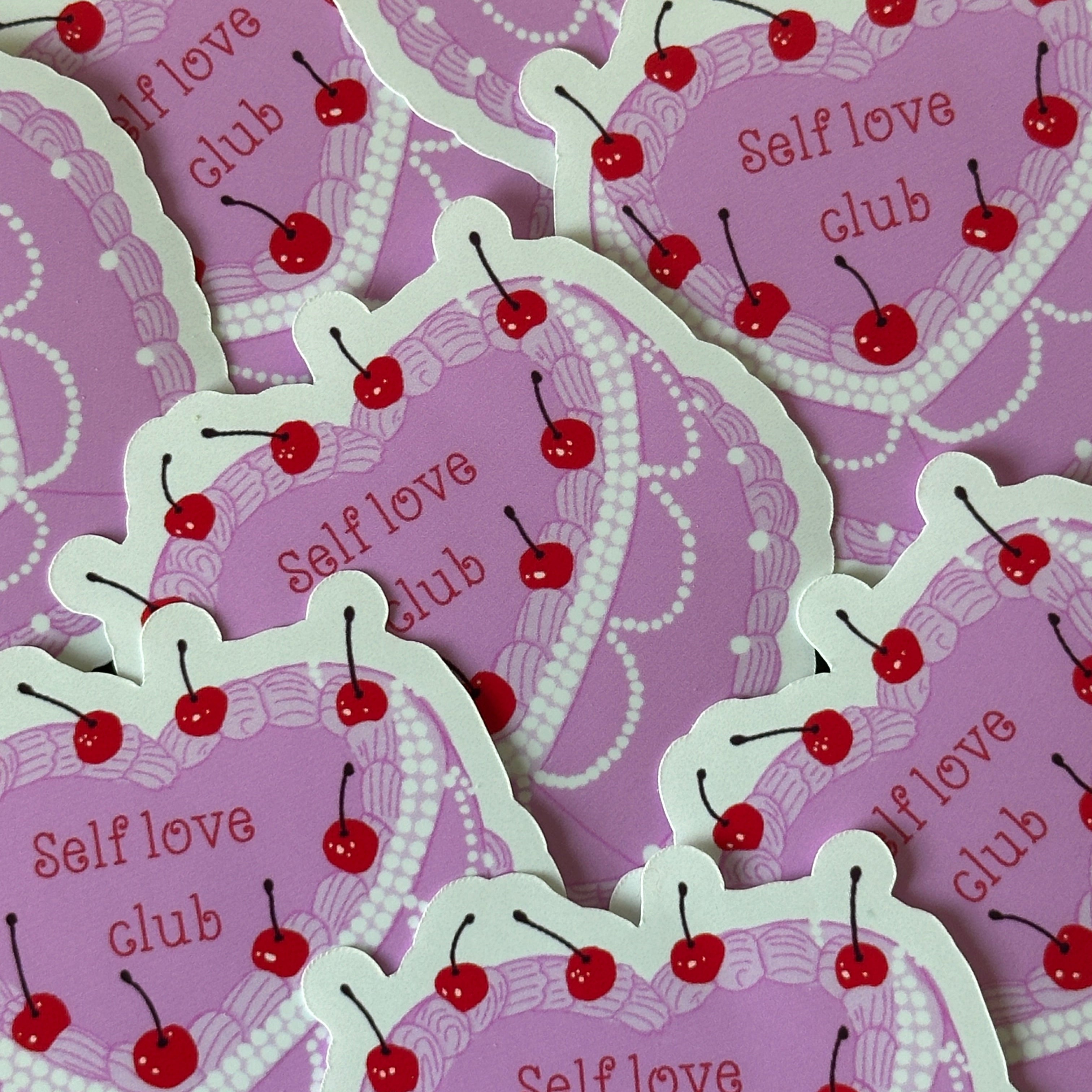 "Glossy pink die-cut vinyl sticker shaped like a cherry-topped cake with pearl trim and the words 'Self love club'"