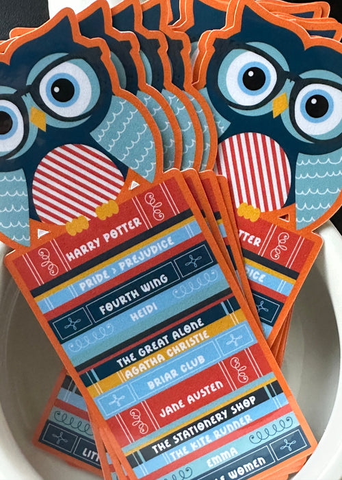 "Die-cut paper bookmark featuring an owl wearing glasses perched on a colorful stack of book spines with titles like Harry Potter, Pride and Prejudice, and Fourth Wing"