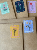 Five floral postage-stamp stickers in mint, navy, lavender, mustard, and blue on kraft paper envelopes