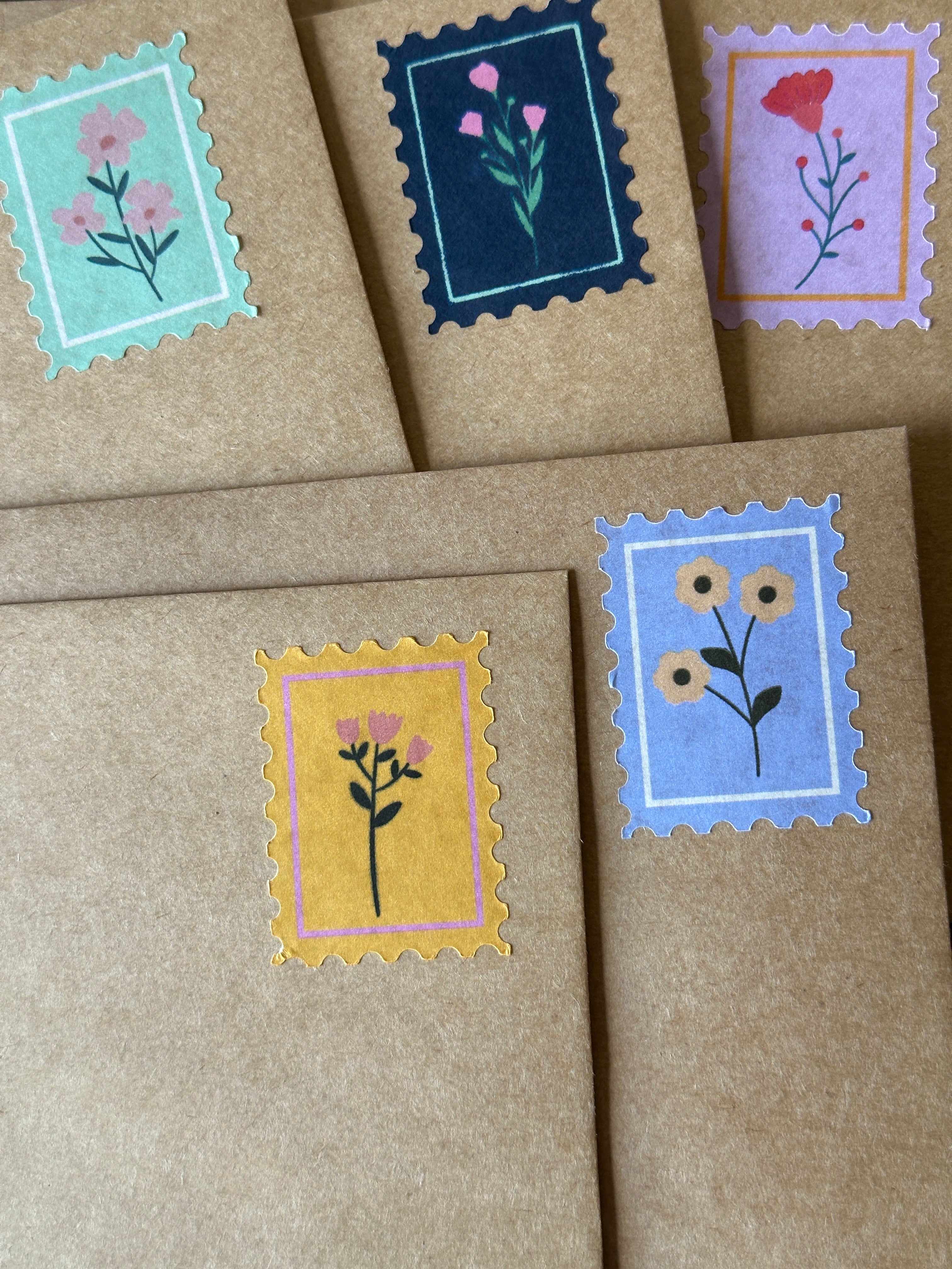 Five floral postage-stamp stickers in mint, navy, lavender, mustard, and blue on kraft paper envelopes